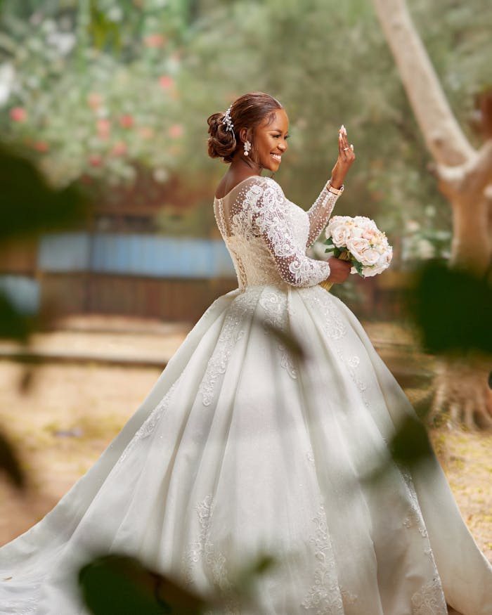 A beautiful bride posing outdoors in an elegant lace wedding dress holding a bouquet.