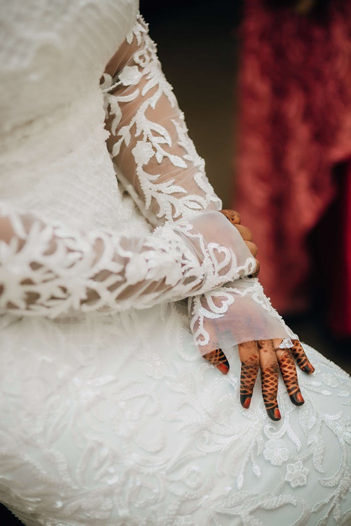 Close-up of a bride in a white lace dress showcasing intricate henna hand designs.